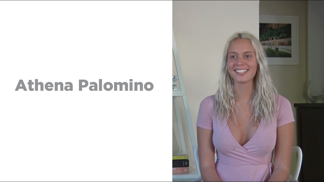 Athena Palomino seated in a purple top beside the original name panel in Dave Naz’s complete interview image